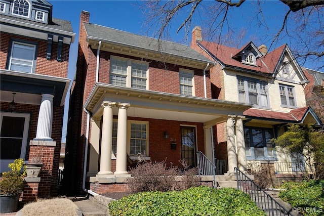 view of front of home featuring a porch, brick siding, and a chimney