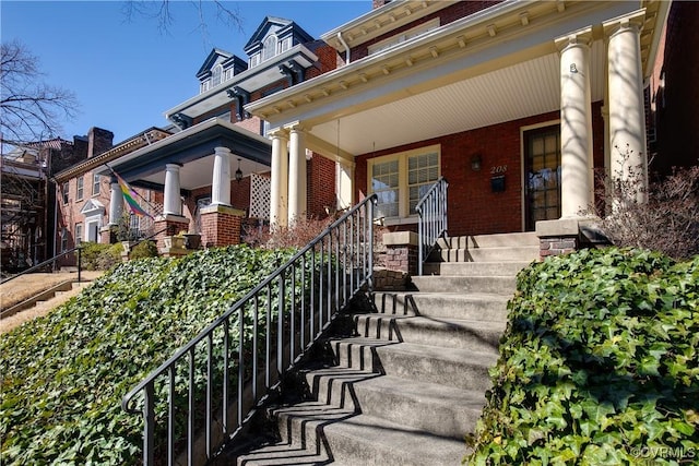 view of exterior entry with brick siding and covered porch