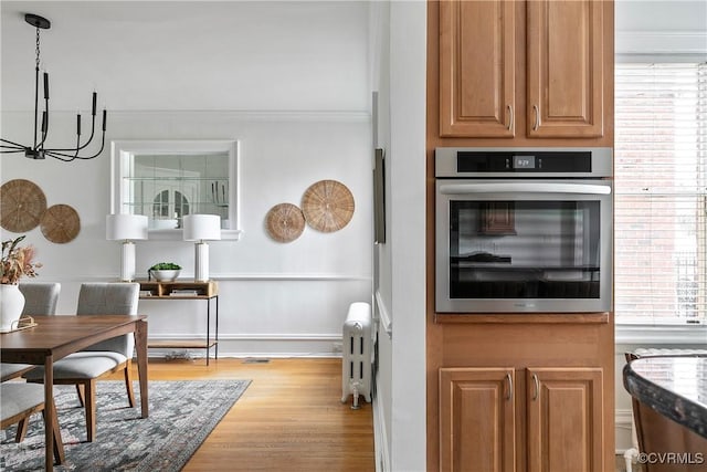 kitchen featuring wood finished floors, an inviting chandelier, radiator heating unit, oven, and pendant lighting