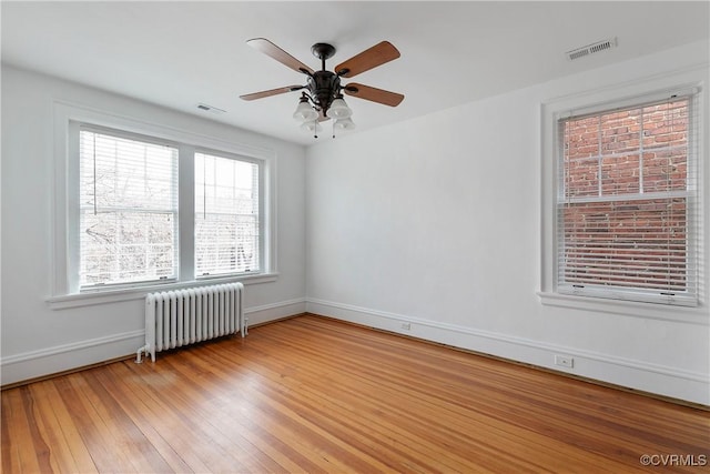 empty room with radiator heating unit, a ceiling fan, visible vents, and light wood-type flooring