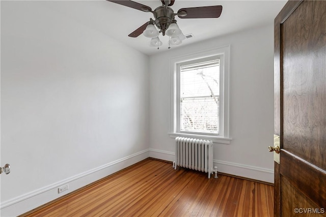 spare room with a ceiling fan, visible vents, baseboards, radiator heating unit, and wood-type flooring