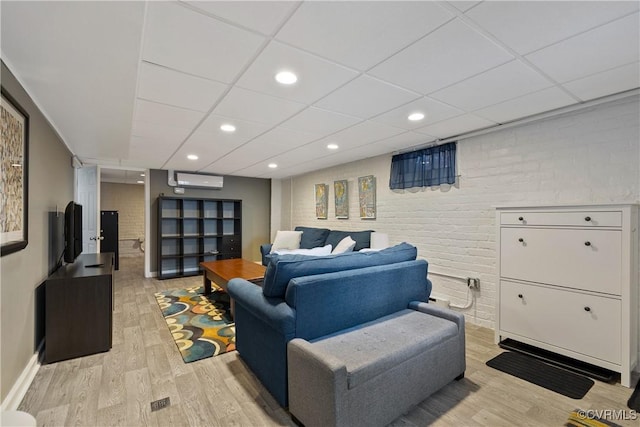 living room with a paneled ceiling, light wood-style flooring, and brick wall