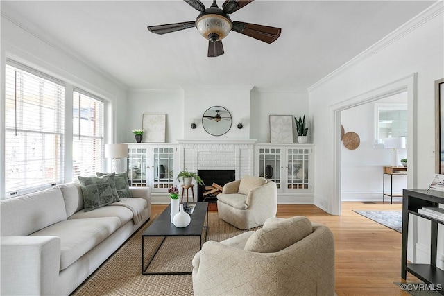 living room featuring light wood-type flooring, baseboards, a brick fireplace, and ornamental molding