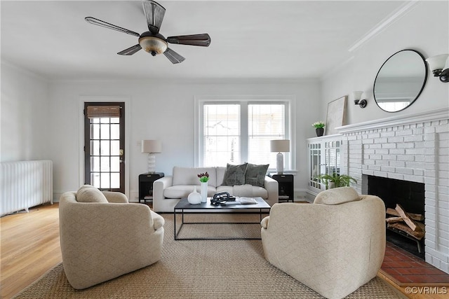 living room featuring radiator, wood finished floors, baseboards, crown molding, and a brick fireplace