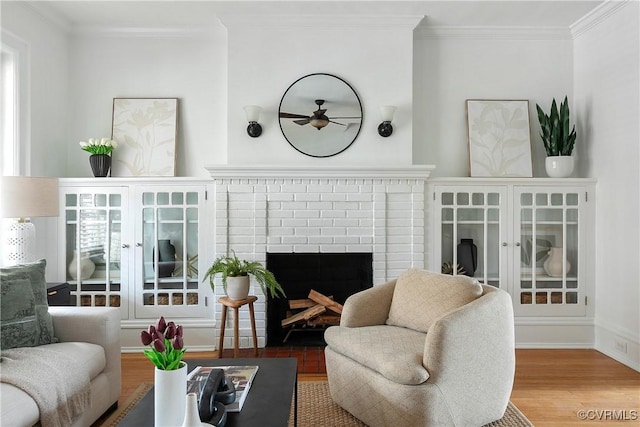 living area with a fireplace, wood finished floors, baseboards, and ornamental molding