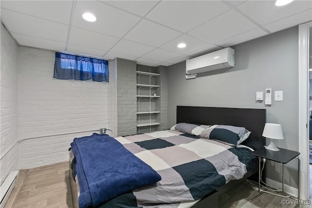 bedroom with brick wall, a baseboard heating unit, an AC wall unit, wood finished floors, and a paneled ceiling