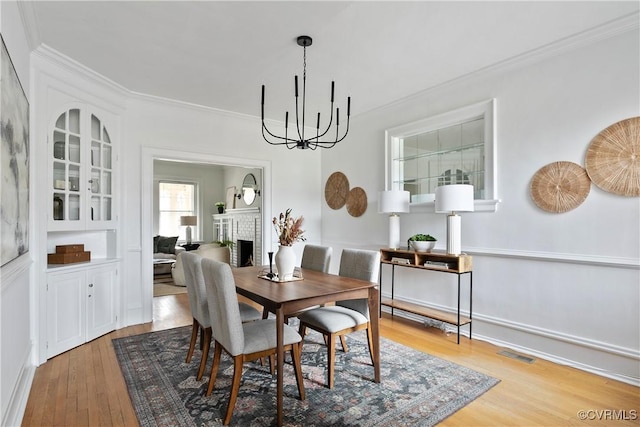 dining area featuring visible vents, an inviting chandelier, a fireplace, hardwood / wood-style flooring, and crown molding