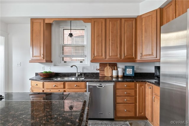 kitchen with brown cabinets, stainless steel appliances, dark stone counters, and a sink