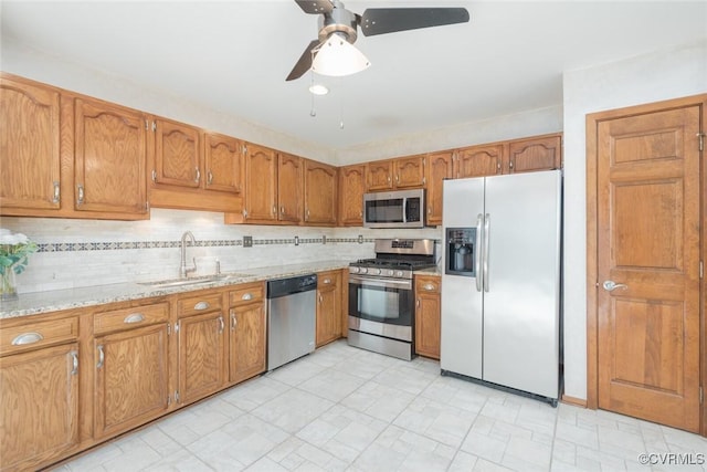 kitchen featuring brown cabinets, a sink, light stone counters, backsplash, and appliances with stainless steel finishes