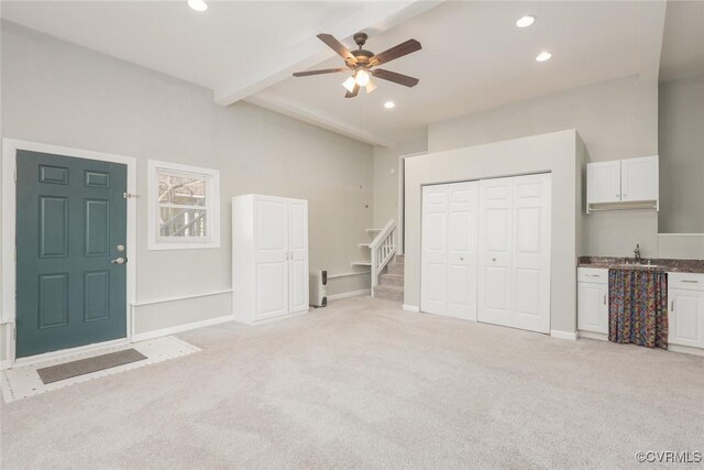 interior space featuring a ceiling fan, beamed ceiling, light colored carpet, and a sink