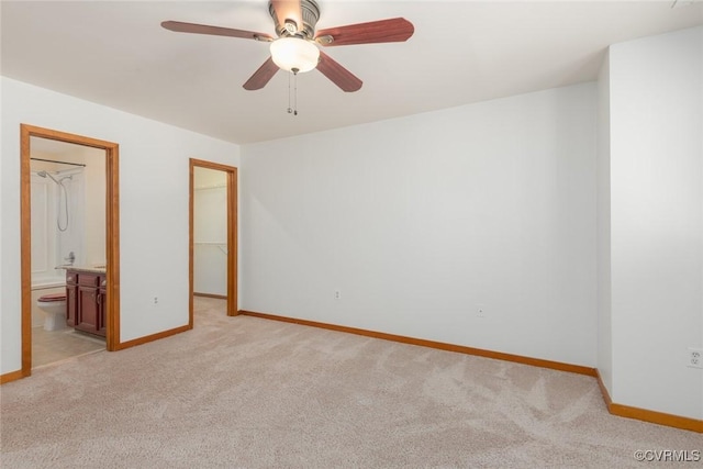 unfurnished bedroom featuring a walk in closet, light carpet, baseboards, and ensuite bath