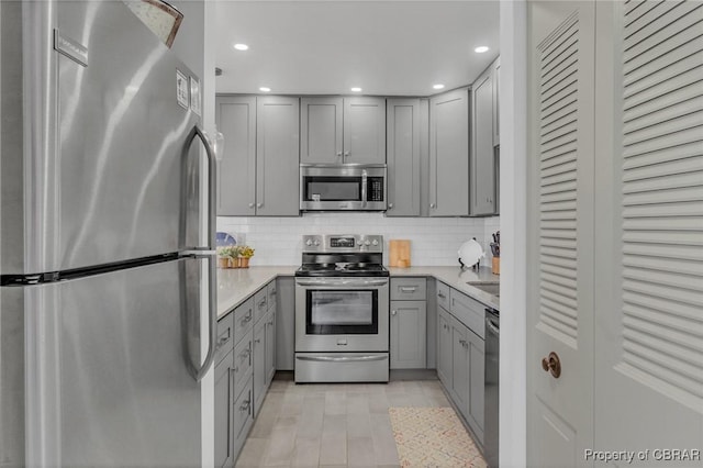 kitchen with recessed lighting, gray cabinets, light countertops, appliances with stainless steel finishes, and backsplash