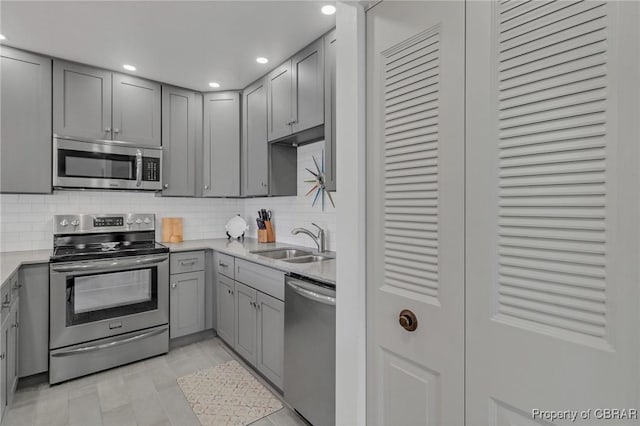 kitchen featuring recessed lighting, gray cabinets, a sink, decorative backsplash, and stainless steel appliances