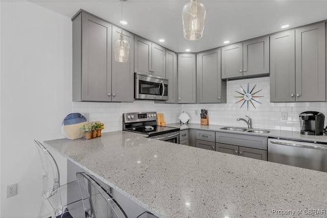 kitchen with gray cabinets, appliances with stainless steel finishes, light stone countertops, and a sink