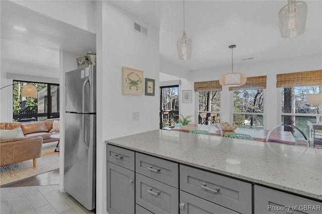 kitchen featuring light stone counters, visible vents, gray cabinets, freestanding refrigerator, and open floor plan