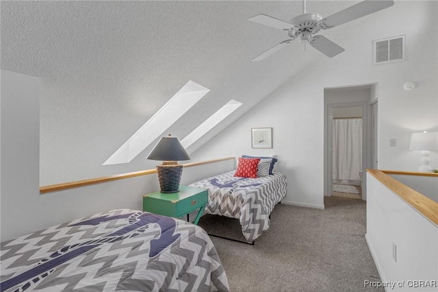 carpeted bedroom featuring visible vents, vaulted ceiling with skylight, a textured ceiling, and ceiling fan