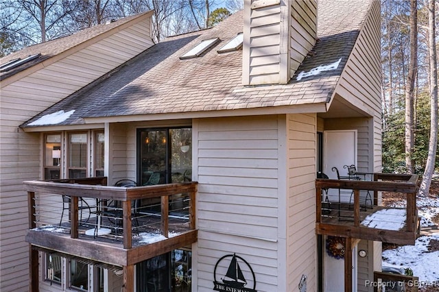 view of side of property featuring a deck, a chimney, and roof with shingles