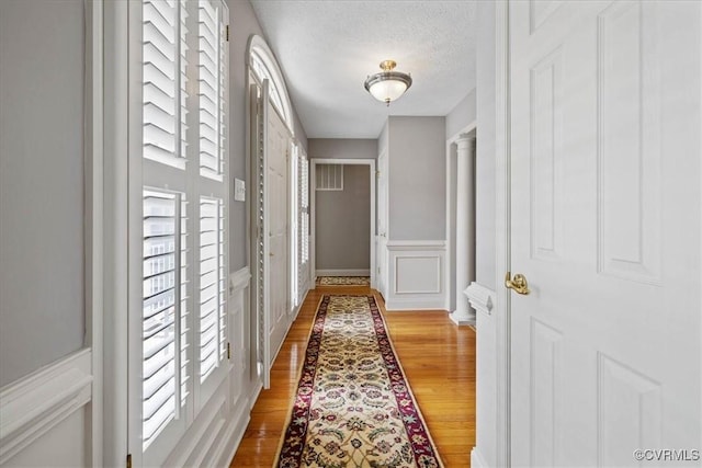 hallway featuring a decorative wall, a textured ceiling, and wood finished floors