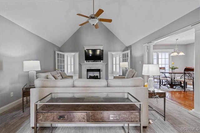 living room featuring ceiling fan, a fireplace, wood finished floors, and decorative columns