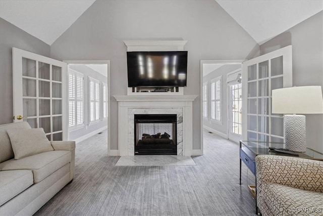 living area featuring high vaulted ceiling, carpet, a high end fireplace, and baseboards