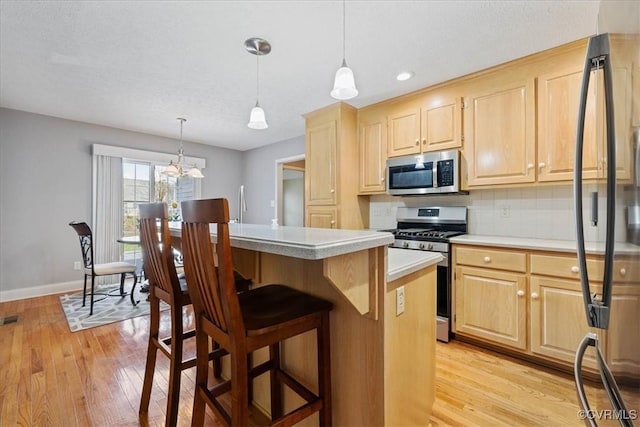 kitchen with light wood-style flooring, a breakfast bar area, appliances with stainless steel finishes, light brown cabinetry, and backsplash