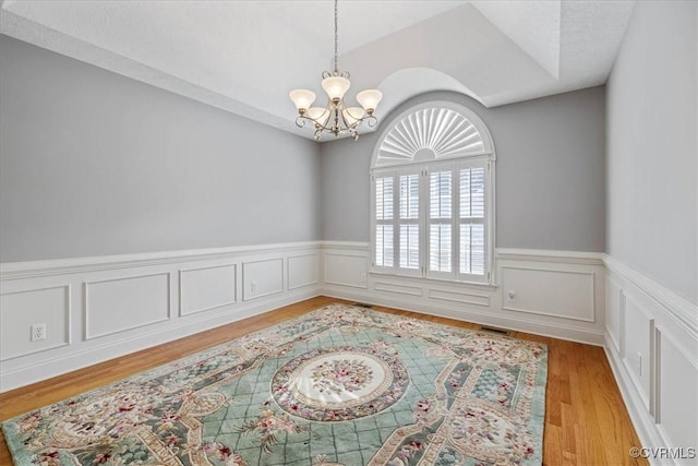 empty room with light wood-style floors, a chandelier, and a wainscoted wall