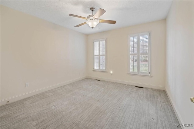 empty room featuring light carpet, baseboards, visible vents, a ceiling fan, and a textured ceiling