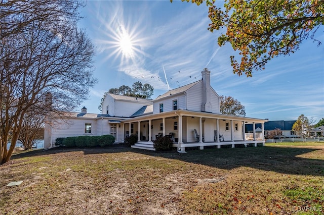 rear view of house featuring covered porch, a chimney, fence, and a yard