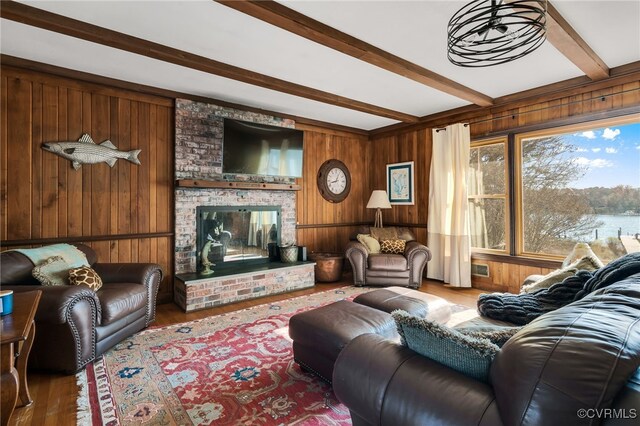 living room with wooden walls, a fireplace, beam ceiling, and wood finished floors