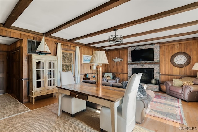 living area featuring a fireplace, wooden walls, beamed ceiling, and wood finished floors