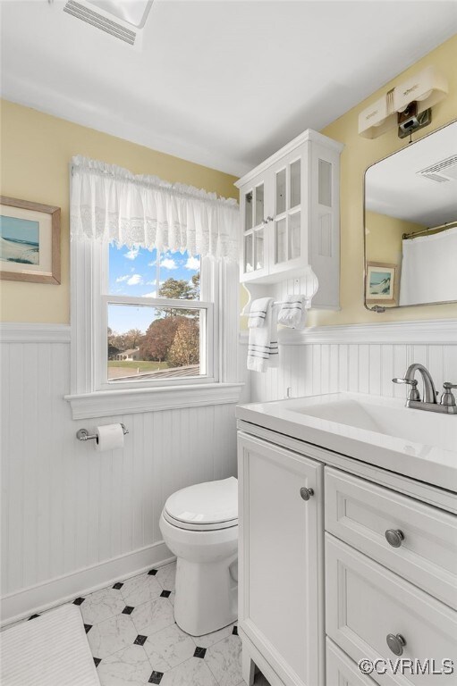 bathroom featuring visible vents, wainscoting, vanity, and toilet