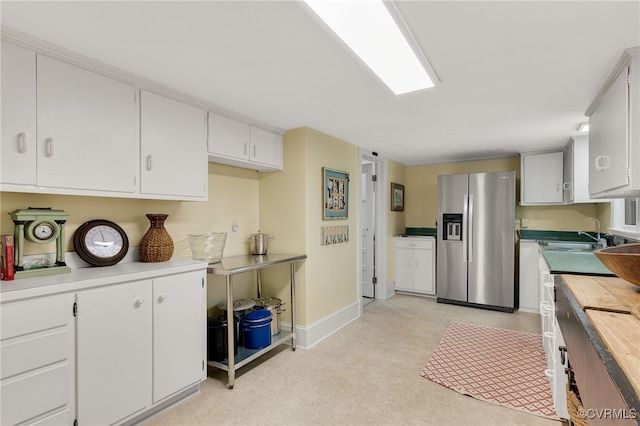 kitchen featuring a sink, white cabinetry, baseboards, wooden counters, and stainless steel fridge