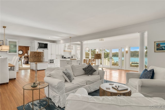 living room with french doors, crown molding, light wood finished floors, a water view, and ornate columns