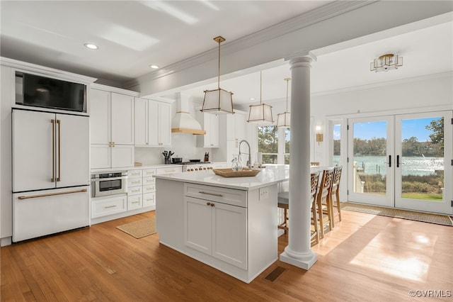 kitchen with stainless steel oven, custom exhaust hood, built in refrigerator, and decorative columns