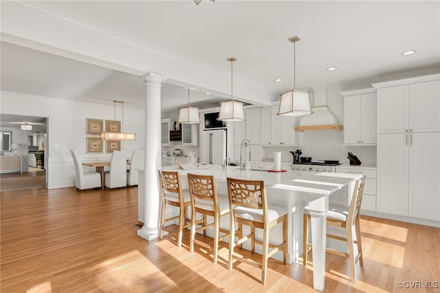 kitchen featuring a breakfast bar area, light wood-style flooring, light countertops, custom exhaust hood, and ornate columns