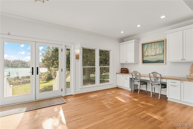 interior space featuring light wood finished floors, white cabinetry, crown molding, and built in study area