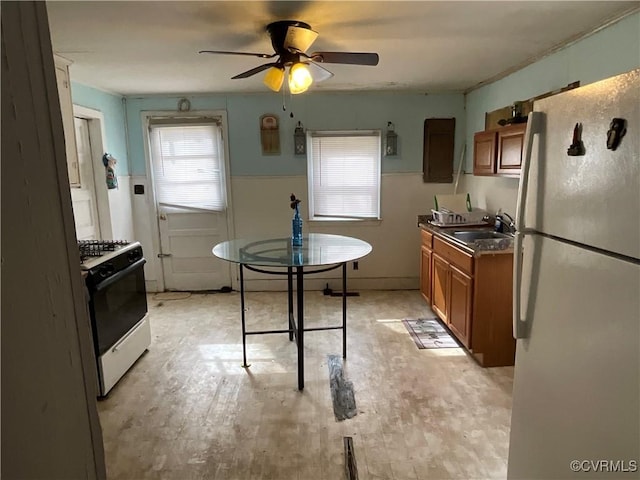 kitchen featuring brown cabinets, light wood-style floors, a sink, ceiling fan, and white appliances