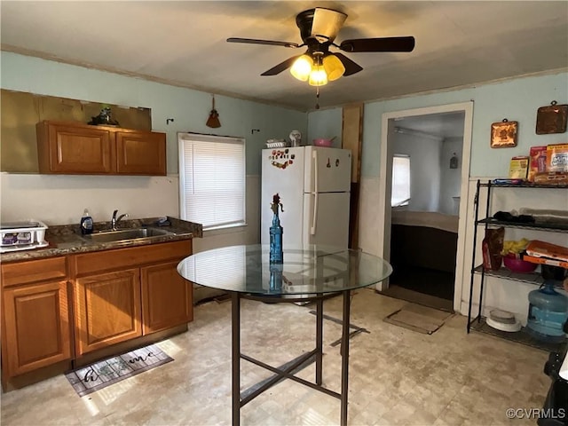 kitchen with light floors, brown cabinetry, a sink, and freestanding refrigerator