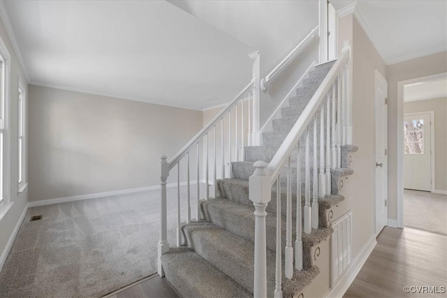 staircase featuring carpet floors, wood finished floors, visible vents, baseboards, and ornamental molding