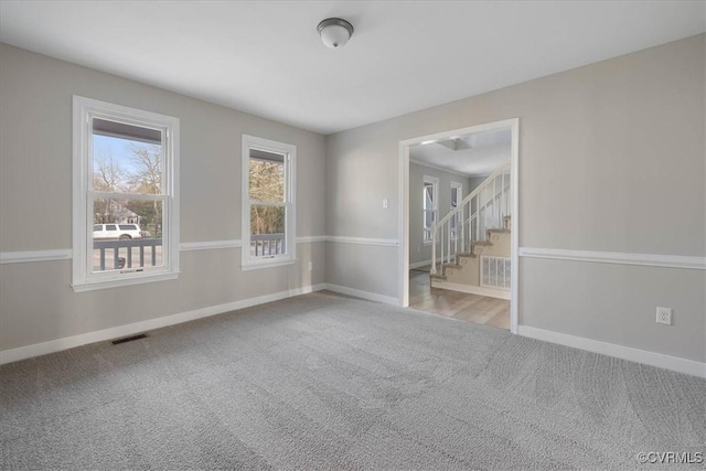 empty room featuring stairway, carpet, visible vents, and baseboards