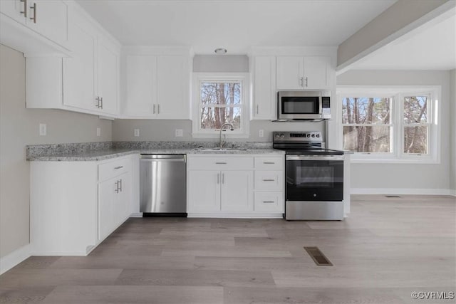 kitchen with light stone countertops, light wood-style floors, appliances with stainless steel finishes, and a sink