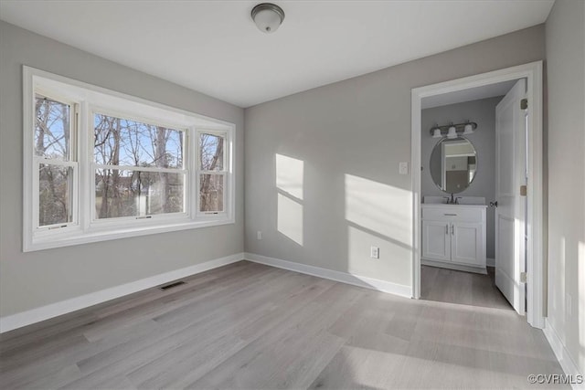 unfurnished bedroom with light wood finished floors, baseboards, visible vents, and a sink