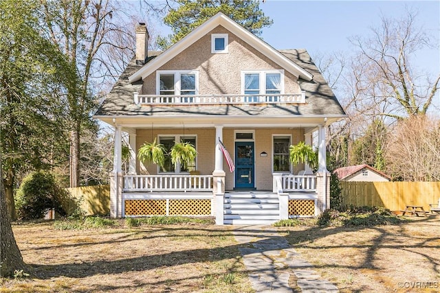 view of front of house with brick siding, fence, a porch, a chimney, and a balcony