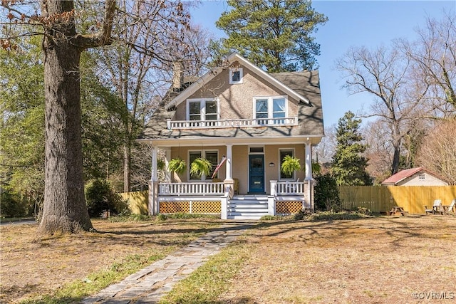 view of front facade featuring a balcony, a porch, a chimney, and fence