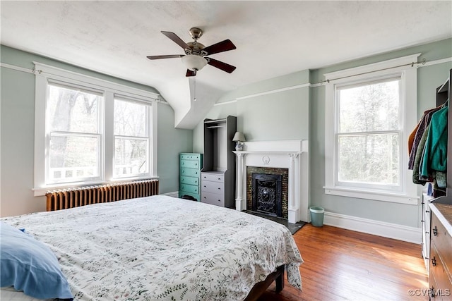 bedroom featuring a ceiling fan, wood finished floors, radiator heating unit, a fireplace, and baseboards