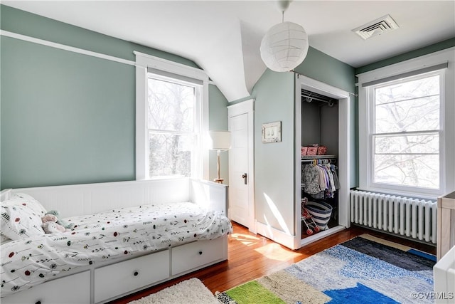 bedroom featuring multiple windows, radiator heating unit, wood finished floors, and visible vents