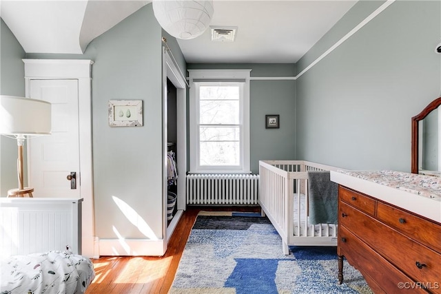 bedroom with visible vents, radiator, and wood finished floors