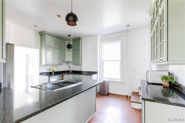 kitchen featuring a sink, wood finished floors, appliances with stainless steel finishes, green cabinets, and hanging light fixtures