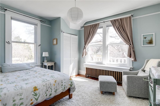 bedroom with a closet, multiple windows, wood finished floors, and radiator heating unit