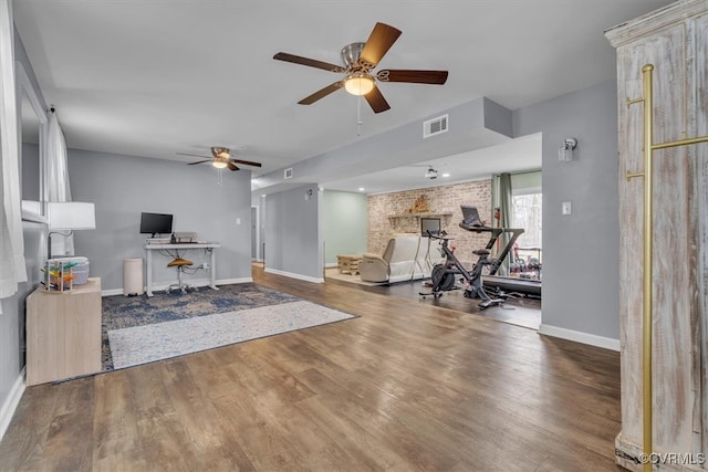 interior space with baseboards, visible vents, brick wall, ceiling fan, and wood finished floors